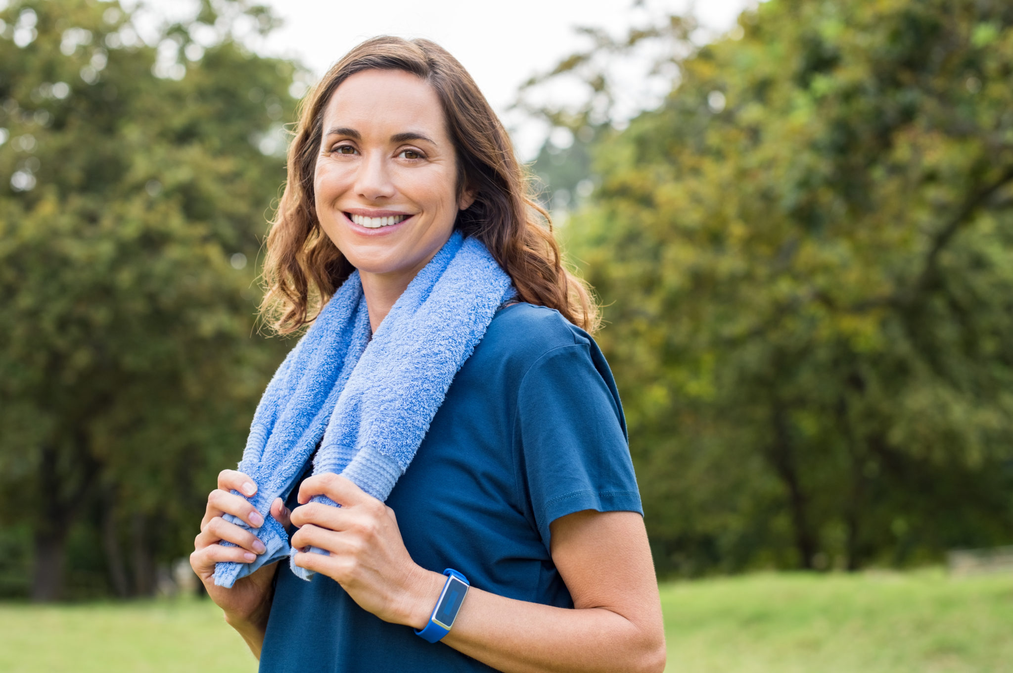 Happy mature woman smiling at park after exercise. Portrait of middle aged woman with blue towel around neck looking at camera. Beautiful mature woman feeling energetic after yoga and exercise outdoor."r