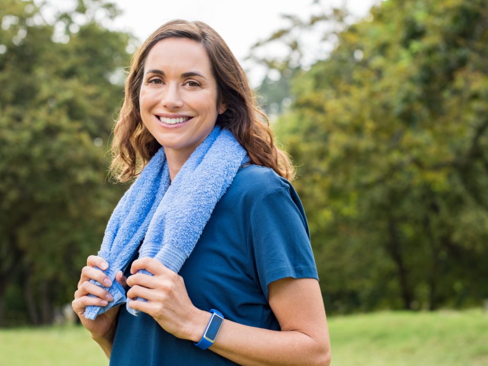 Mature fitness woman smiling Happy mature woman smiling at park after exercise. Portrait of middle aged woman with blue towel around neck looking at camera. Beautiful mature woman feeling energetic after yoga and exercise outdoor.